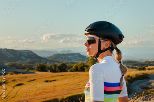 Fit young female professional athlete, wearing cycling suit, standing, looking at the horizon of the mountains.