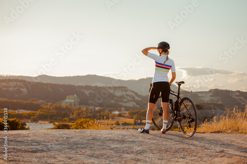 Fit young female cyclist, standing with her bike in hand, admiring the scenery.