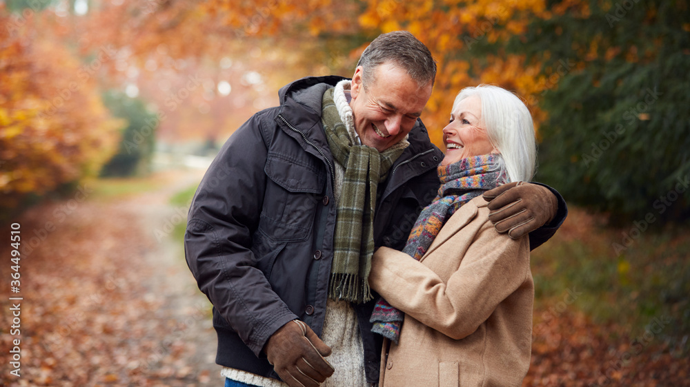 Loving Senior Couple Hugging As They Walk Along Autumn Woodland Path Through Trees Loving Senior Couple Hugging As They Walk Along Autumn Woodland Path Through Trees