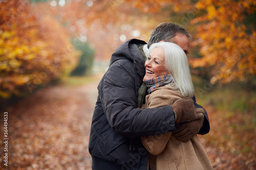 Loving Senior Couple Hugging As They Walk Along Autumn Woodland Path Through Trees