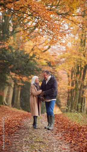 Loving Senior Couple Holding Hands As They Walk Along Autumn Woodland Path Through Trees Together © Monkey Business