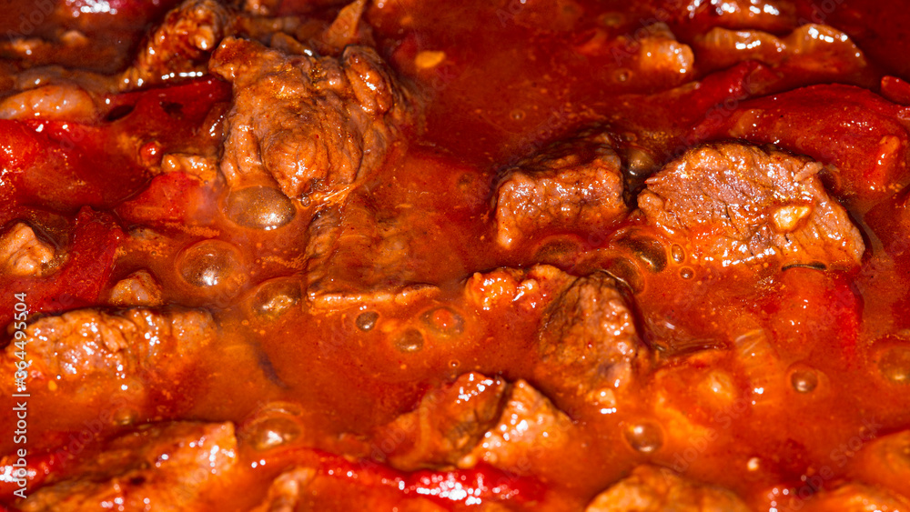 Traditional Hungarian goulash. Boiling beef stew with tomatoes and paprika, macro picture.