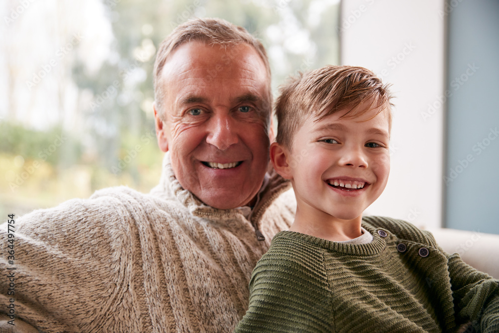 Portrait Of Grandson Sitting On Sofa At Home With Grandfather Portrait Of Grandson Sitting On Sofa At Home With Grandfather