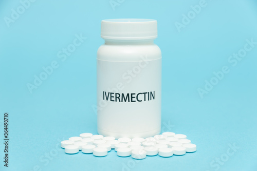 Treatments for Coronavirus (COVID-19): IVERMECTIN in white bottle packaging with scattered pills. Isolated on blue background. Horizontal shot.
