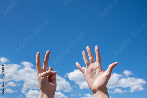 Close-up of female hands showing seven fingers on a blue sky background. Number seven in sign language. Copy space