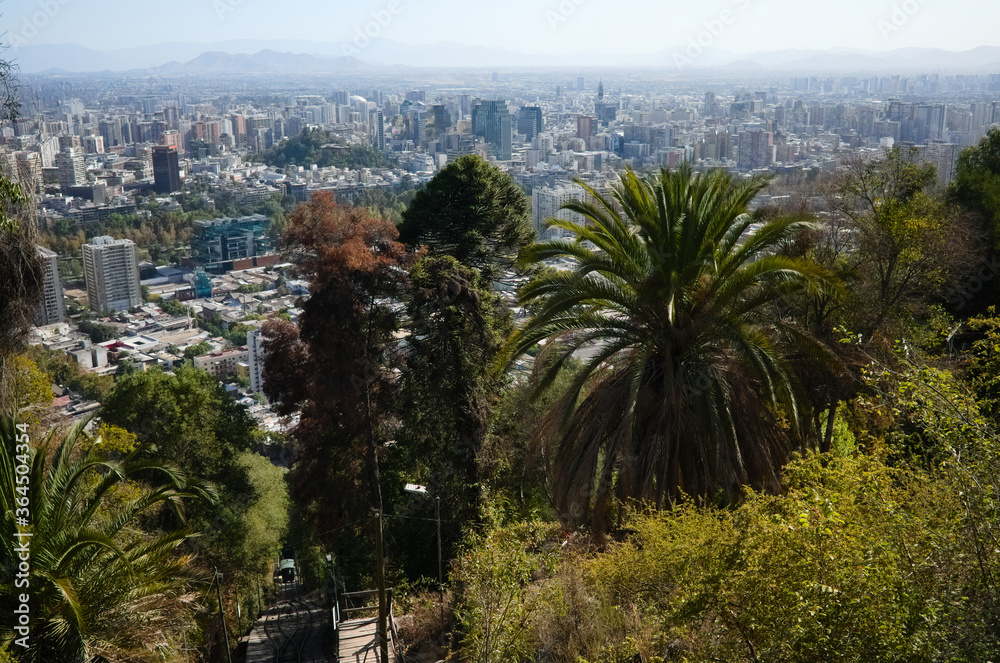 Santiago de Chile panoramic city view from San Cristobal hill with lush foliage with palm trees and funicular road. Santiago, Chile