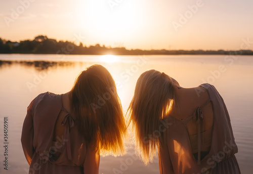 Obraz na płótnie Young girls with long hairs enjoying sunrise by the river. Back view w salonie