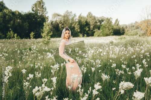 Obraz na płótnie Young woman in beatiful dress walking with mirror in flowering meadow w salonie