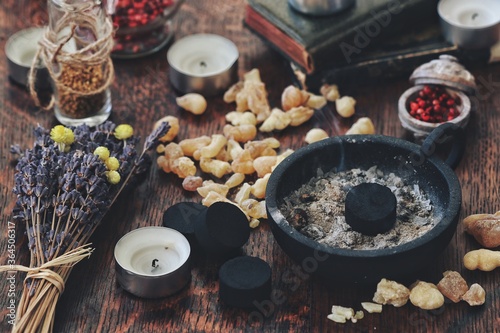 Many little pieces of light yellow Yemen frankincense resin incense on dark wooden table. Charcoal disk in black holder ready for air cleansing ceremony on a busy and cluttered wiccan witch altar photo