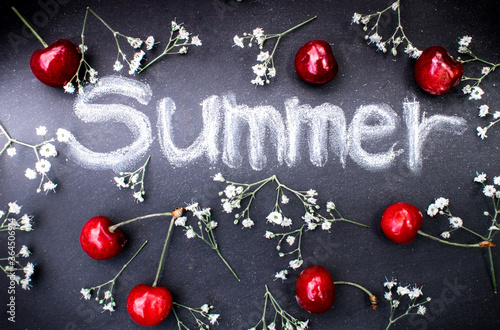Black board written with the inscription summer with white chalk. Decorated with red cherries and white tiny flowers