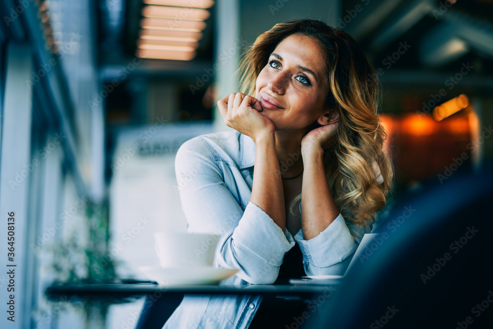 Young happy hipster girl dressed in trendy outfit dreaming while sitting at table in coffee shop.Gorgeous pondering female blogger thinking about new ideas for content in personal website indoors Young happy hipster girl dressed in trendy outfit dreaming while sitting at table in coffee shop.Gorgeous pondering female blogger thinking about new ideas for content in personal website indoors