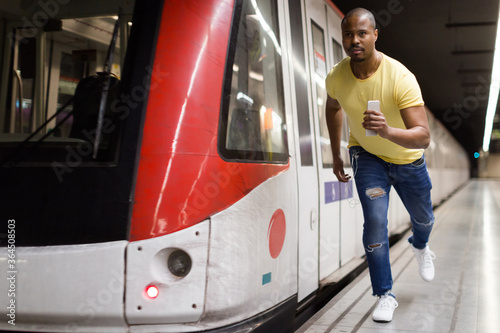 Young latino man passenger running to train at metro station platform..