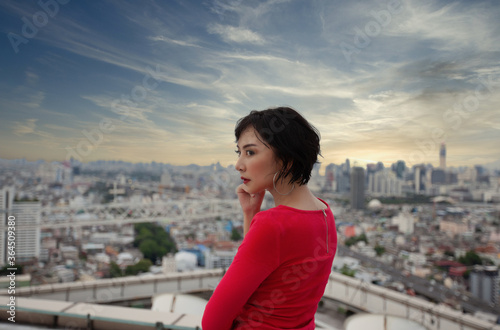 Portrait of a businesswoman in a red dress is watching the top of the office building at sunset. © panyajampatong