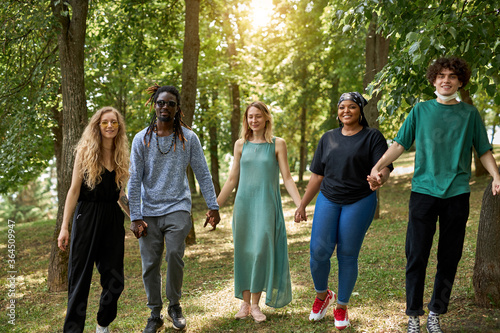 happy diverse african and caucasian people walk together in the park, have conversation and laugh. tolerance, international friendship concept