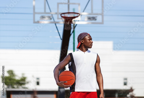 Serious black basketballer holding ball at outdoor sports court, blank space