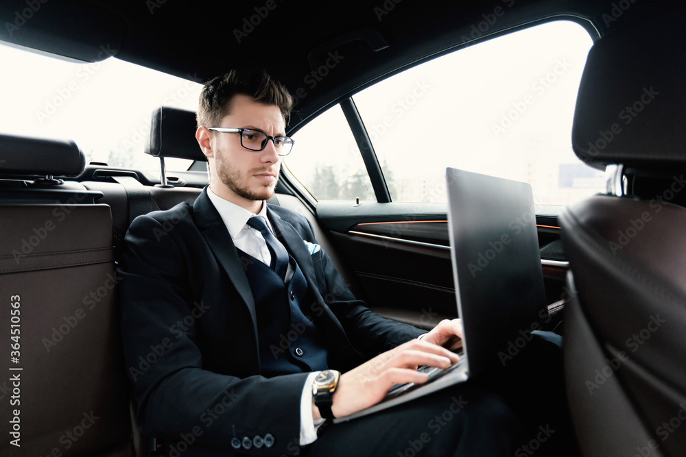 Busy serious businessman using his laptop in luxury car