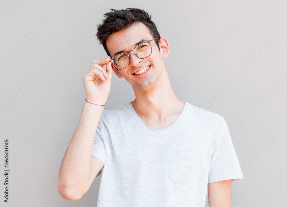 A portrait of young handsome man in grey t-shirt isolated on gray background touching his glasses. A portrait of young handsome man in grey t-shirt isolated on gray background touching his glasses.