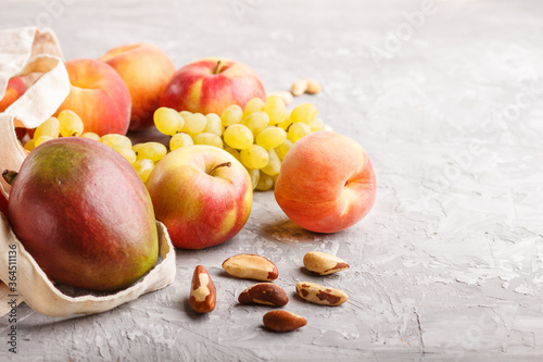 Fototapeta Naklejka Na Ścianę i Meble -  Fruits in reusable cotton textile white bag on a gray concrete background. Zero waste shopping, storage and recycling concept. Side view, close up, copy space.