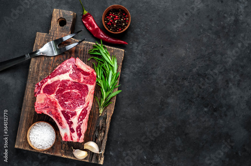 Raw cowboy steak. Marbled beef meat with spices on a stone background