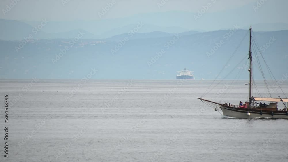 Small wooden tourist boat passing by in Adriatic Sea. In the distance big cargo ship and mountains. Long, static shot Small wooden tourist boat passing by in Adriatic Sea. In the distance big cargo ship and mountains. Long, static shot
