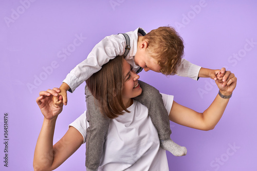 playful little caucasian boy hugs her mother neck and looks at her with a smile, parent and chil in love, happy