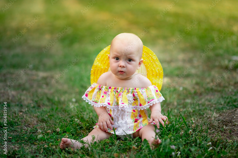 baby girl 10 months old sitting on the grass in summer in a yellow dress, walking in the fresh air baby girl 10 months old sitting on the grass in summer in a yellow dress, walking in the fresh air