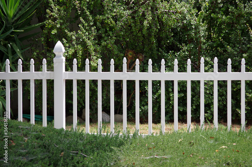Close view of a section of a white picket fence with green bushes behind
