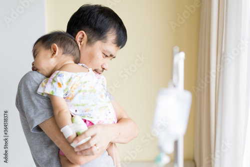 Asian father is hugging and holding his baby to relax with love while the child admit as inpatient in the hospital, concept of parent take care to their sickness child in family lifestyle.