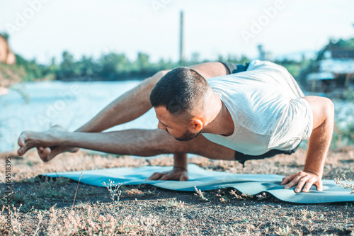 A young man sits on a quarry lake at sun, doing yoga. Sitting in yoga pose. Balance, harmony, concentration and relaxation.
