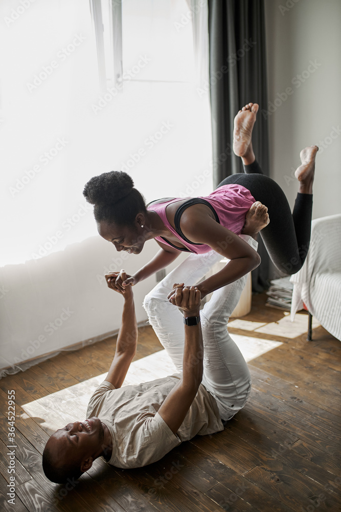 Fototapeta premium adult african man holding slender woman on his legs, the do sport exercises together at home