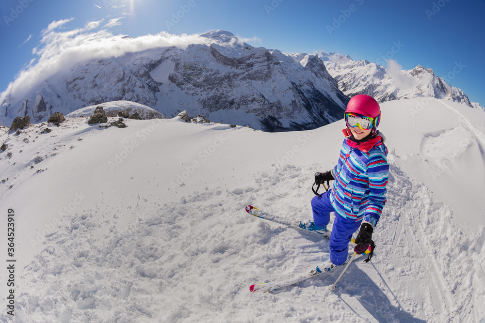 Portrait from above of a girl on ski stand in snow on top of a mountain view and look up wearing pink helmet