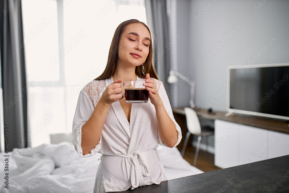 attractive young caucasian lady is enjoying smell of hot coffee, woman inhales aroma of coffee in bedroom attractive young caucasian lady is enjoying smell of hot coffee, woman inhales aroma of coffee in bedroom