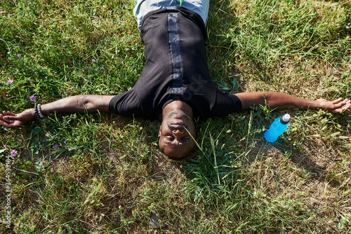 African sportsman resting in a park with an isotonic drink.