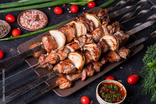 Fresh, home-cooked on the grill fire meat beef shish kebab with vegetables and spices, with barbecue sauce and ketchup, on a dark background. Shish kebabs - grilled meat and vegetables Lamb Skewers