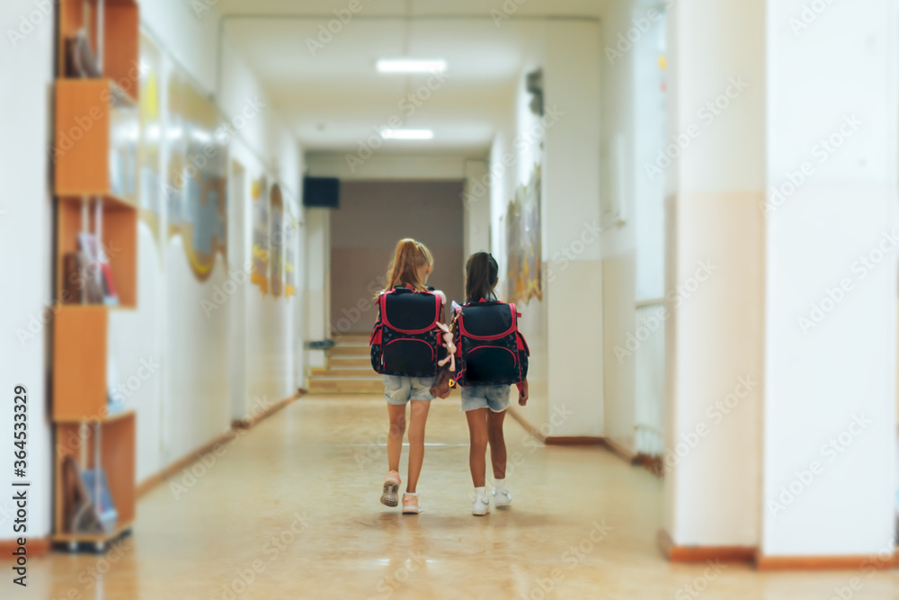 Two schoolgirls holding each other's hands are walking along the school corridor. Two schoolgirls holding each other's hands are walking along the school corridor.