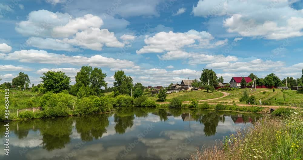 Village landscape with a small lake, time lapse of clouds reflected in the water, beautiful summer landscape