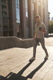 stylish guy, wearing glasses, climbs the steps to the office check-in with a phone in his hands. light jeans and fashionable gray T-shirt. beautiful contour sunlight