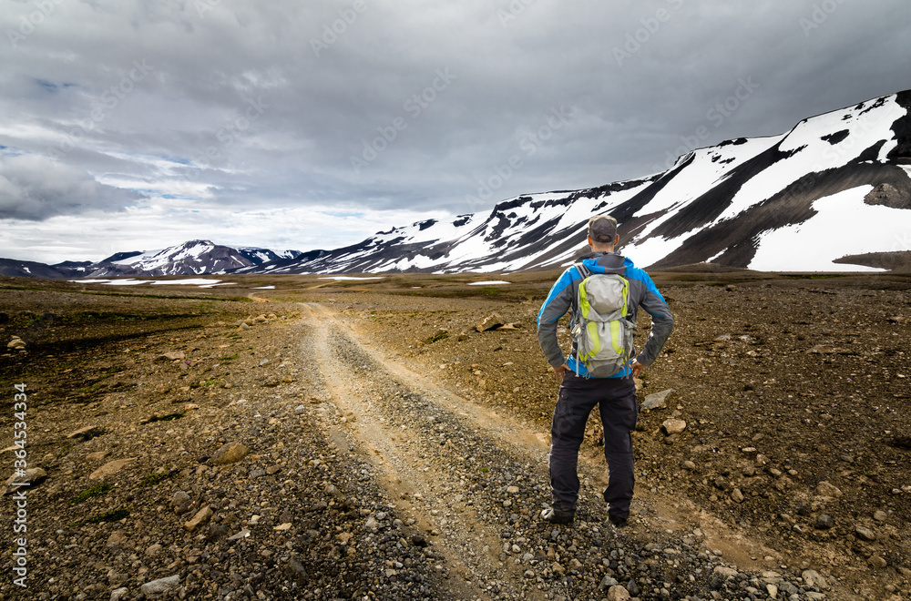 Hiker Man with Backpack standing on hiking trail in snow mountain and arctic desert. Kaldidalur, Thorisjokull, Iceland. View to Thorisdalur.