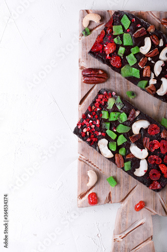 Chocolate bar with dried fruit, sublimated berry and nuts on the wooden board on the white table. Top view