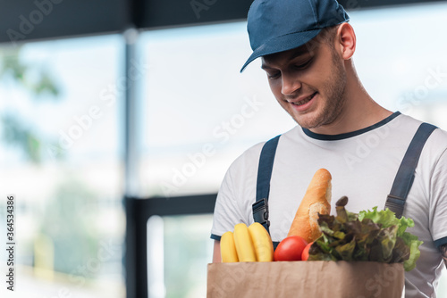 cheerful delivery man holding paper bag with fresh groceries