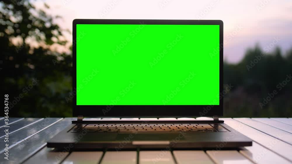 Black laptop with a green screen is on a folding table at sunset on nature in the summer. Black laptop with a green screen is on a folding table at sunset on nature in the summer.
