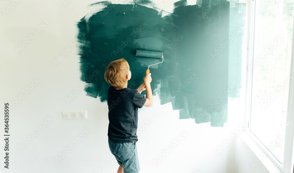 Fototapeta premium Little boy a preschooler paints in the room by the wall roller. The child helps to repair the parents.