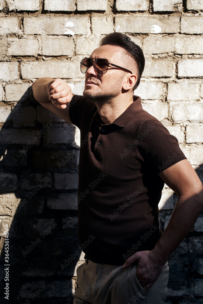 Obraz premium stylish guy with glasses stands near a stone wall and looks away. thought. strong and strict male gaze. sunlight. half-length portrait. looks up