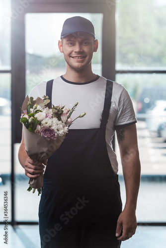 happy delivery man in uniform and cap holding bouquet of flowers