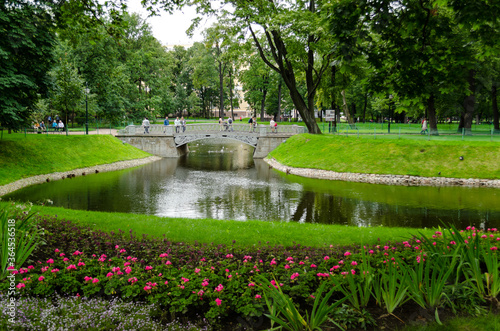 Green garden with a lake. Summer courtyard with lawn. Beautiful summer landscape landscape park. Nature for background on postcard.Taurian Garden, St. Petersburg, Russia, July 17, 2017