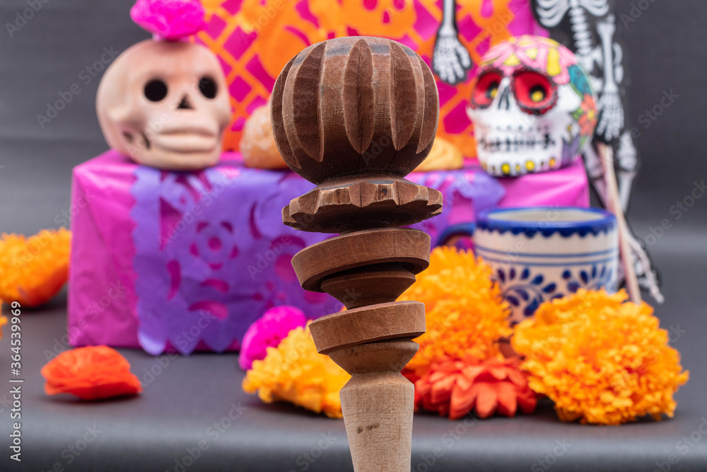 A chocolate grinder and a traditional altar for Mexican Day of the Dead with skulls, flowers and cut paper