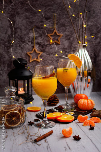 Two glasses of orange juice, cinnamon sticks, black lantern, silver vase, fresh oranges and tangerines on a wooden table