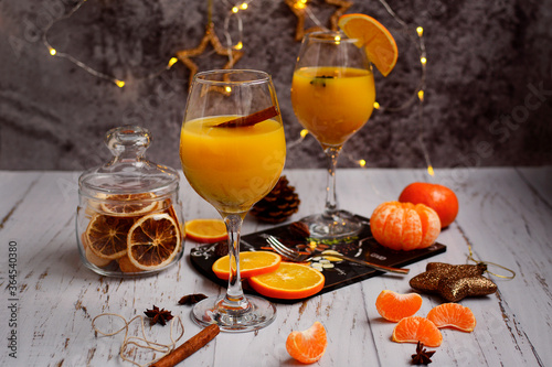 Still life of two glasses with orange juice and slices of tangerines and oranges on the background of New Year's decor