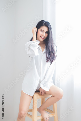A beautiful Asian woman, Thai, wearing a white pajamas, posing sexy in the bedroom in the morning.