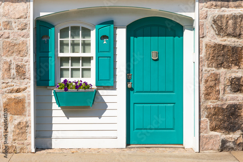 Partial front exterior of white cottage with teal shutters and door and teal window box with purple petunias